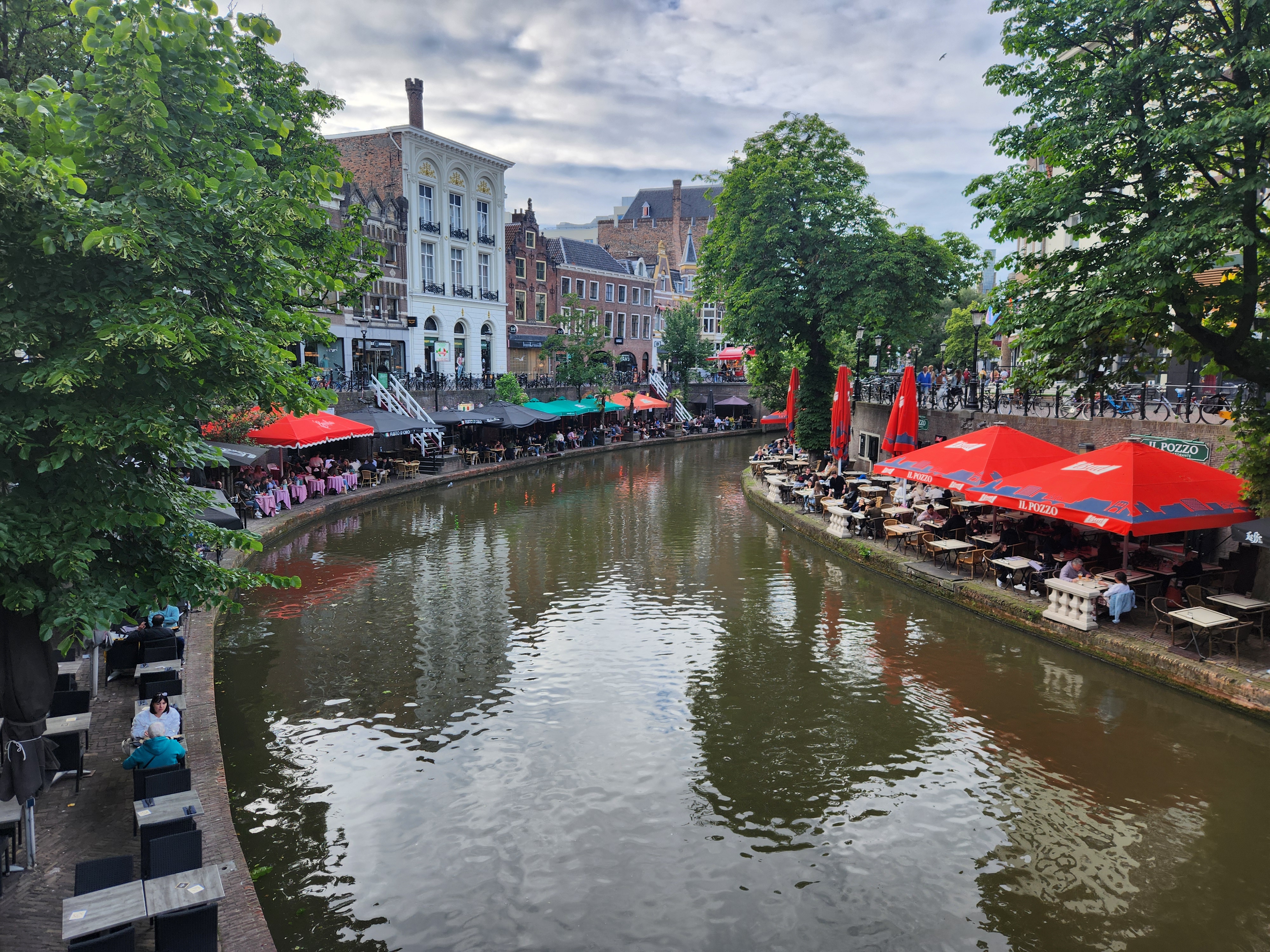 Utrecht city centre, the canal is lower with a bank full of cafe tables and umbrellas, there is then a higher street level with old buildings